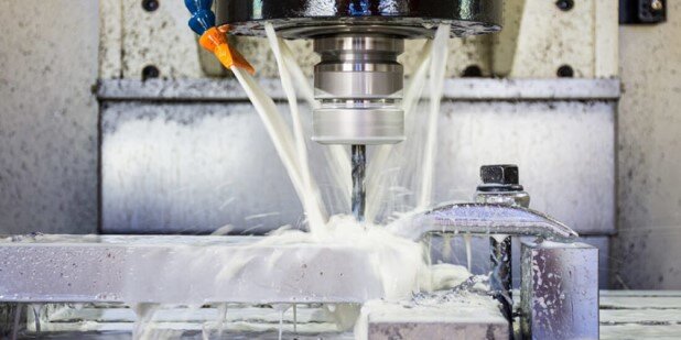 CNC mill cutting a metal part with coolant spray